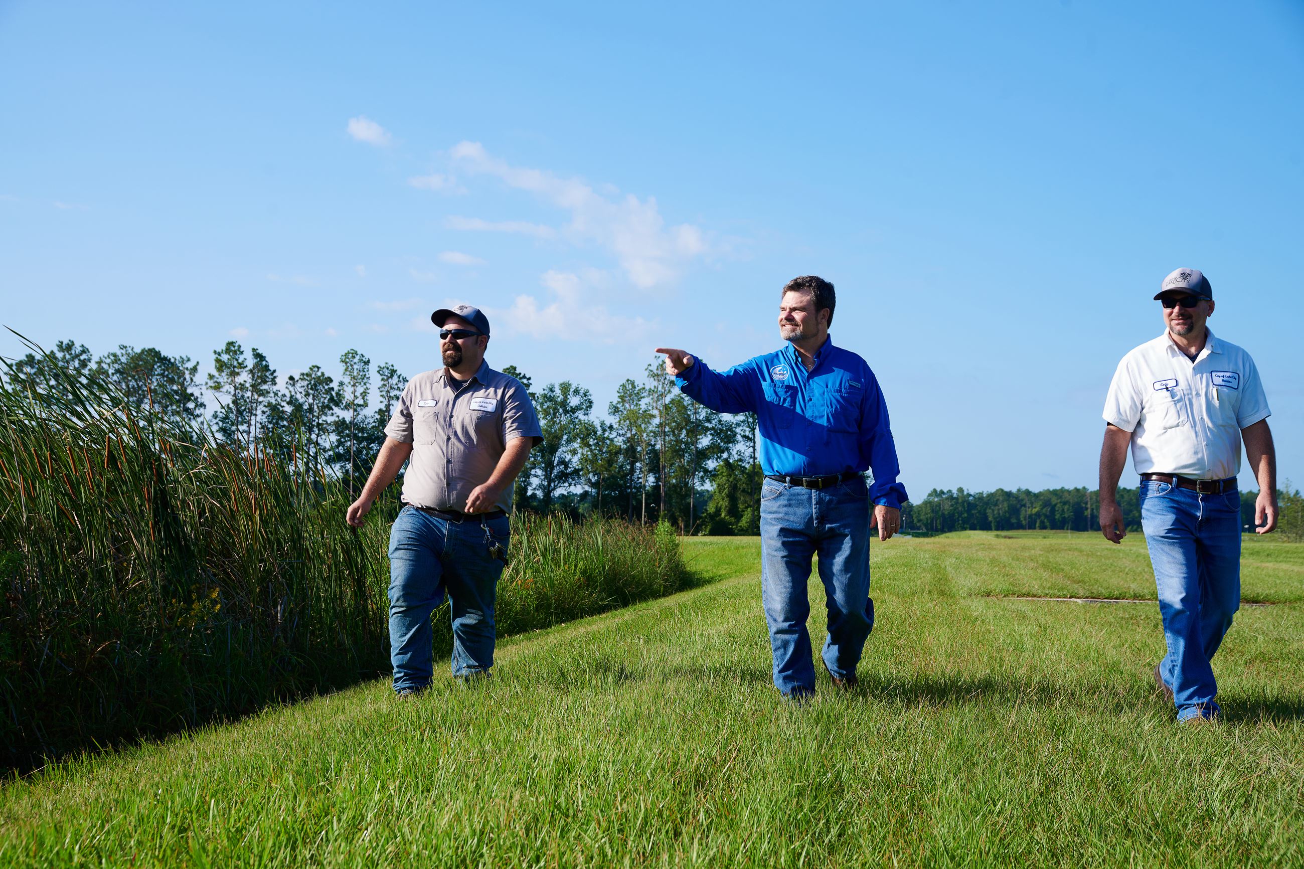 Three people walking through a wetland area with one person pointing